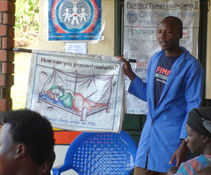 A community volunteer teaches patients about malaria prevention in the clinic waiting room.